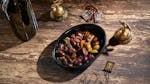 Assorted olives in a black bowl with decorative brass items, creating a rustic feel.