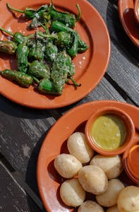 Assorted Spanish tapas with Padron peppers and sauces served on a rustic outdoor table.