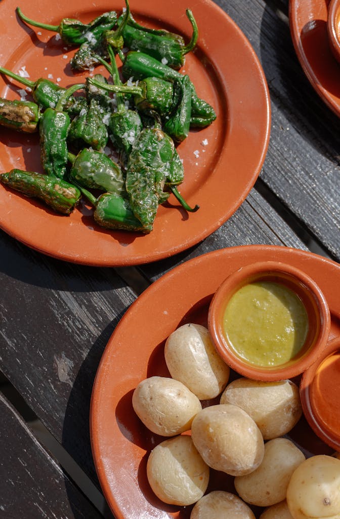 Assorted Spanish tapas with Padron peppers and sauces served on a rustic outdoor table.