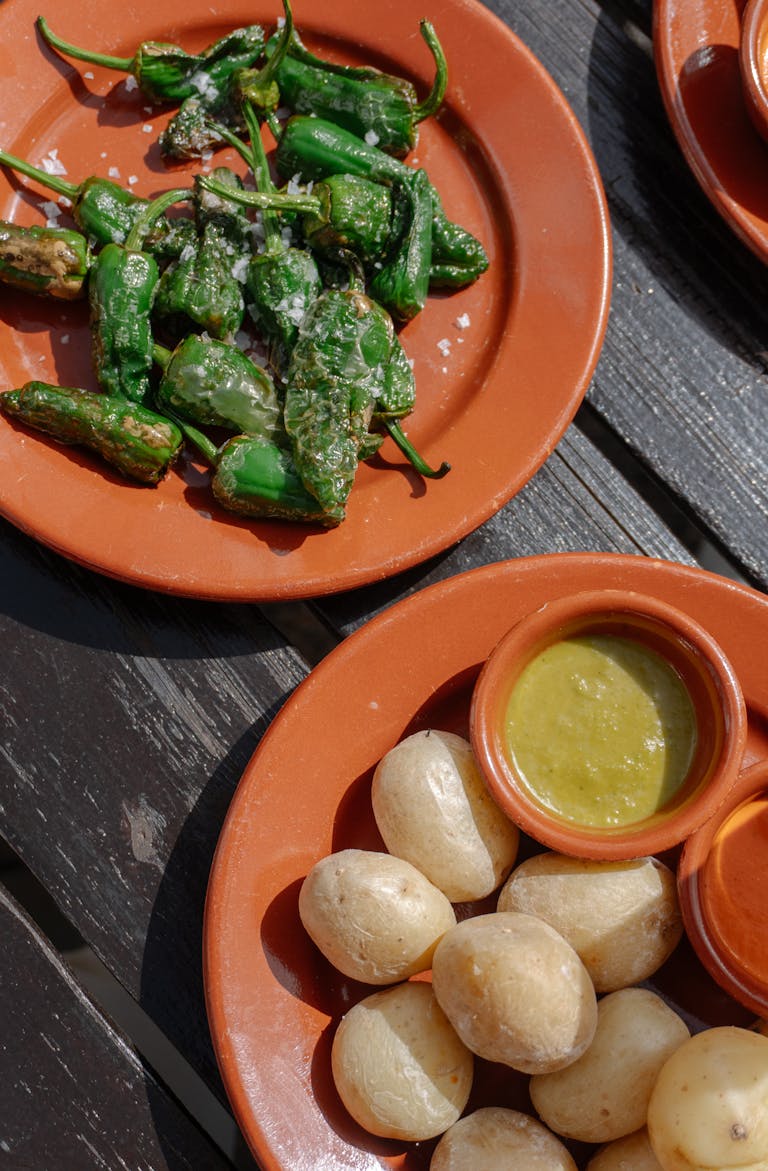 Assorted Spanish tapas with Padron peppers and sauces served on a rustic outdoor table.