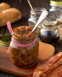 Jar of bacon jam with a spoon, served with bacon strips.