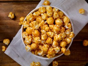 Bowl of caramel popcorn on a napkin on a wooden surface.