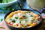 Close-up of a cheesy skillet dish topped with fresh herbs and green onions, perfect for food lovers.