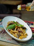 Close-up of a flavorful Italian pasta dish with olive oil being poured, highlighting fresh ingredients.