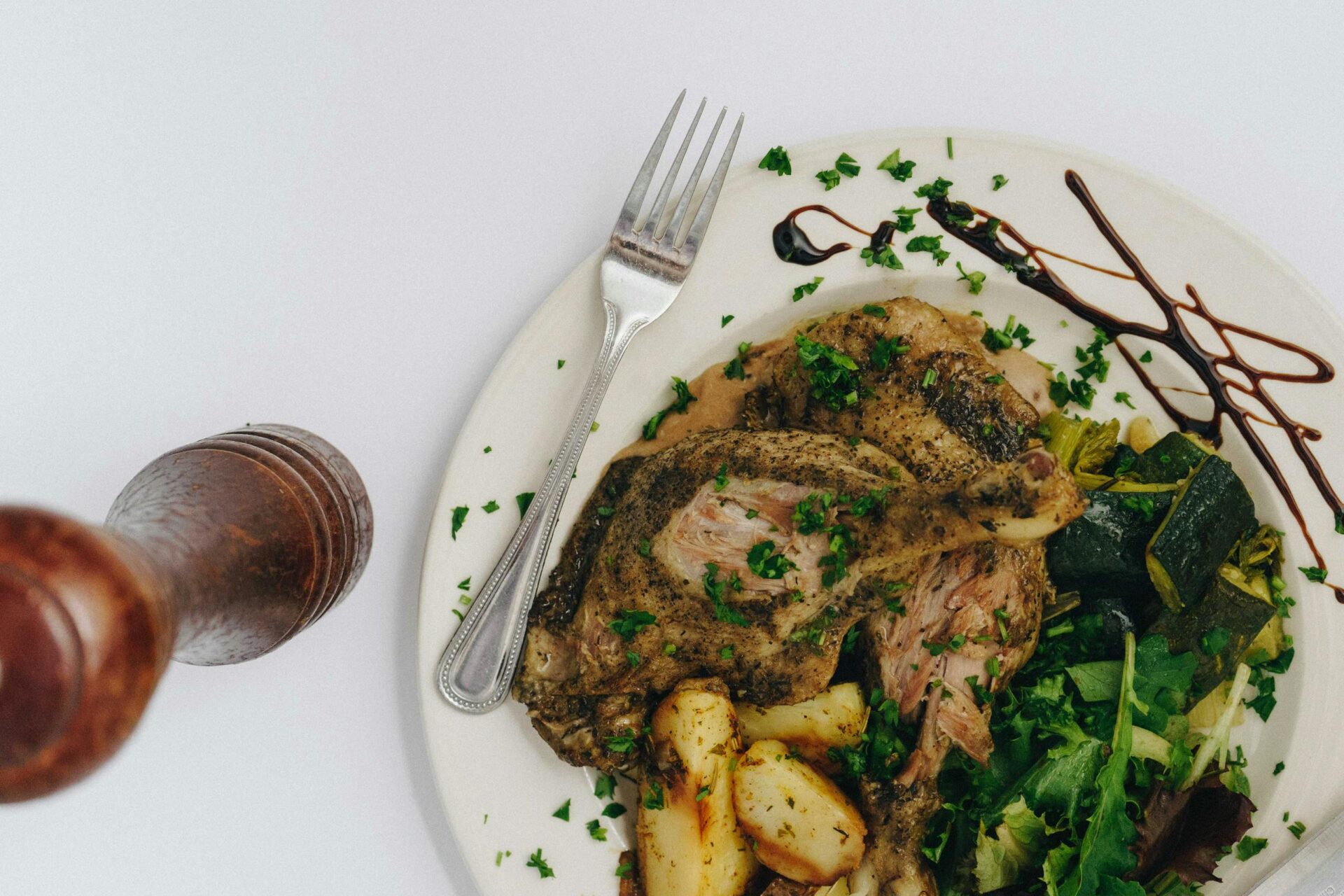 Close-up of a gourmet meal featuring roasted duck, potatoes, zucchini, and greens, garnished with fresh herbs.