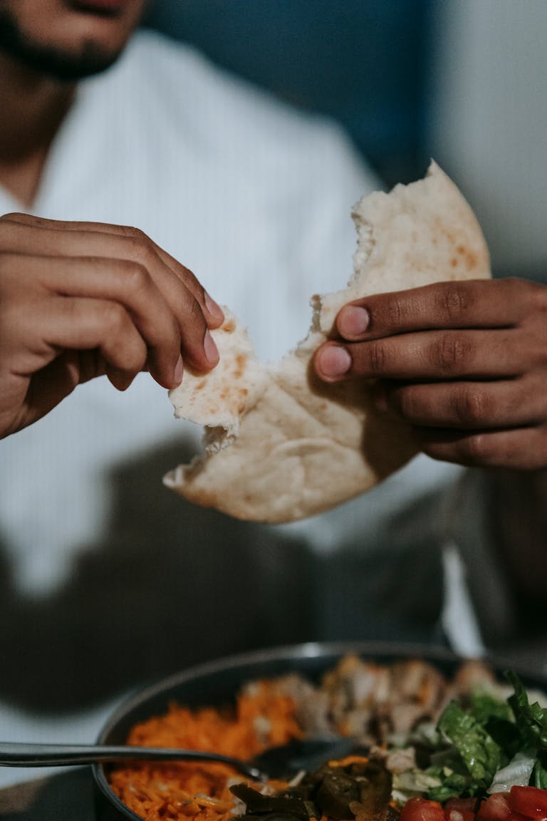Close-up of a man breaking pita bread during an indoor iftar meal.