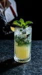 Close-up of a mojito cocktail garnished with fresh mint on a textured surface.