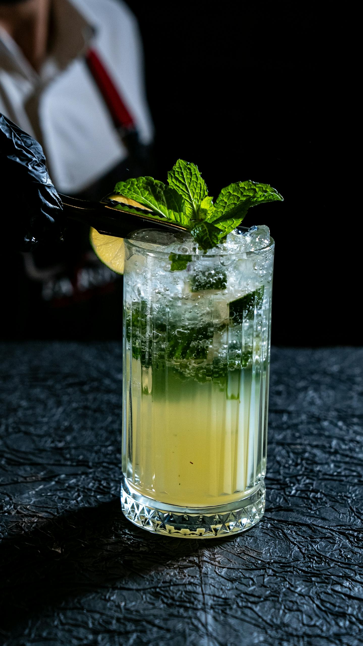Close-up of a mojito cocktail garnished with fresh mint on a textured surface.