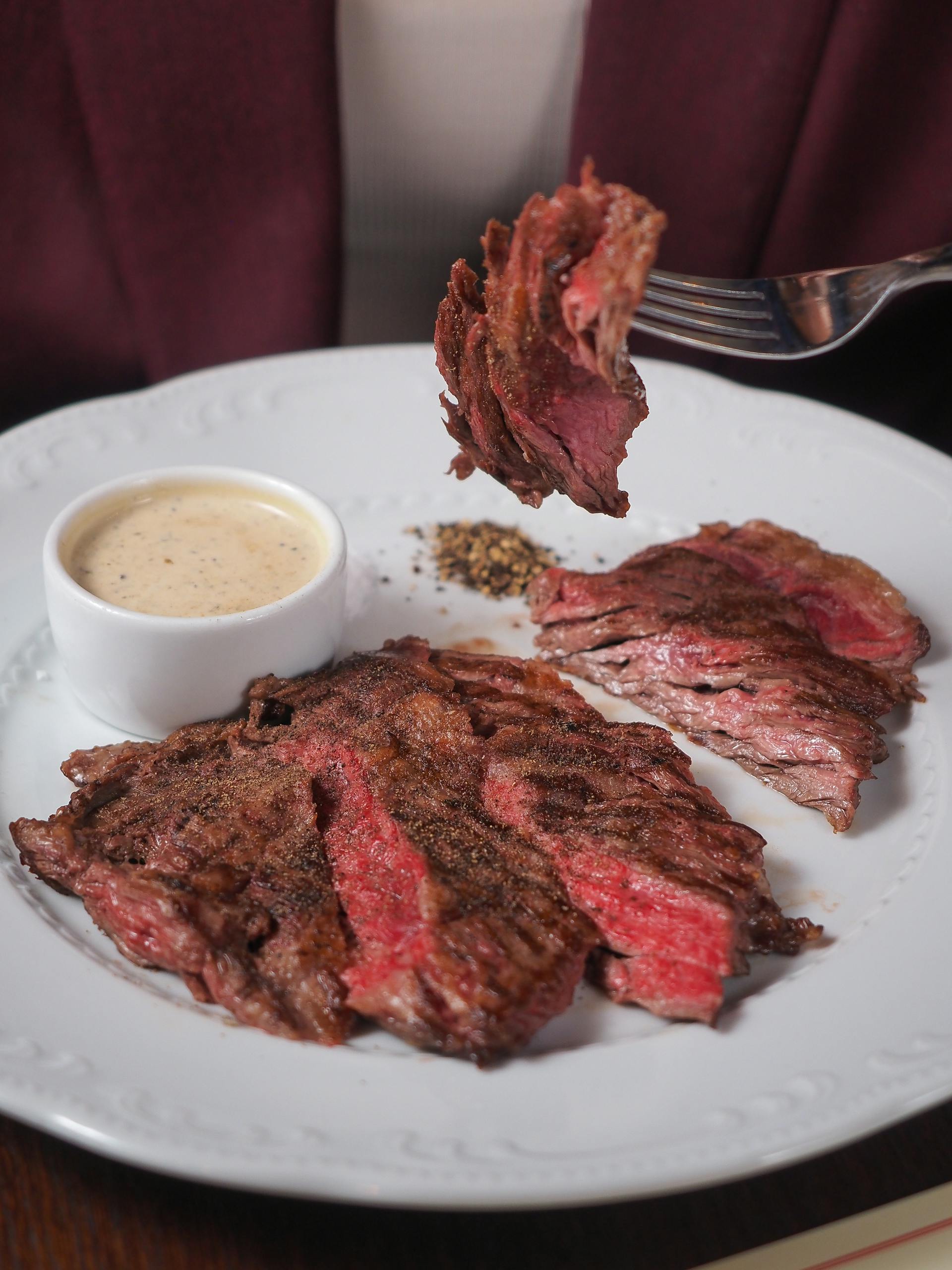 Close-up of a perfectly grilled steak served with creamy sauce and pepper seasoning.