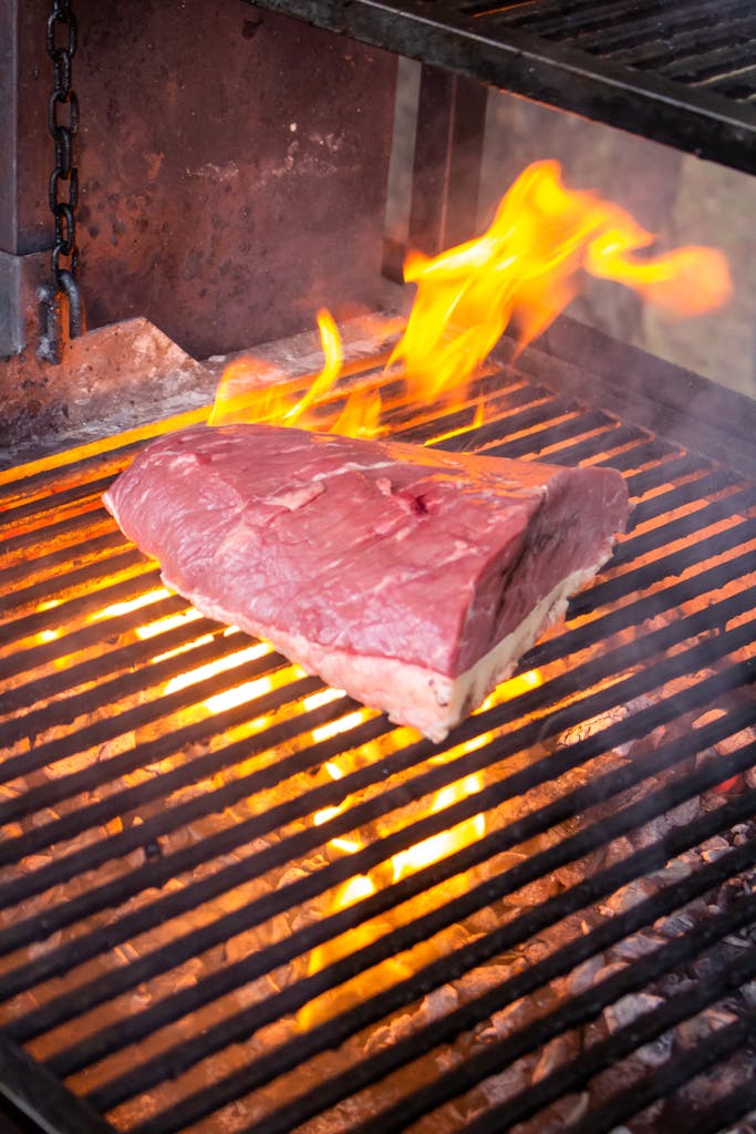 Close-up of a raw beef cut sizzling on a fiery barbecue grill.