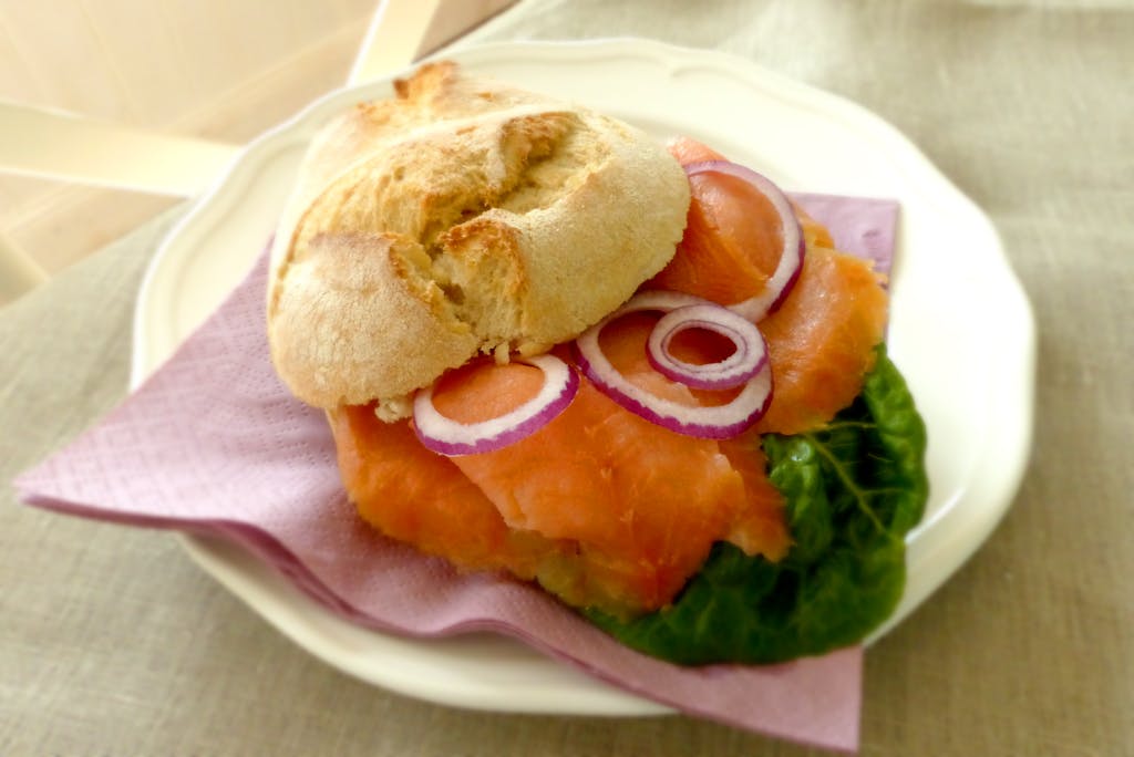 Close-up of a salmon sandwich with fresh vegetables on a ceramic plate, perfect for a healthy meal.