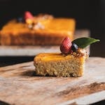 Close-up of a slice of cake topped with strawberries and blueberries on a rustic wooden tray.