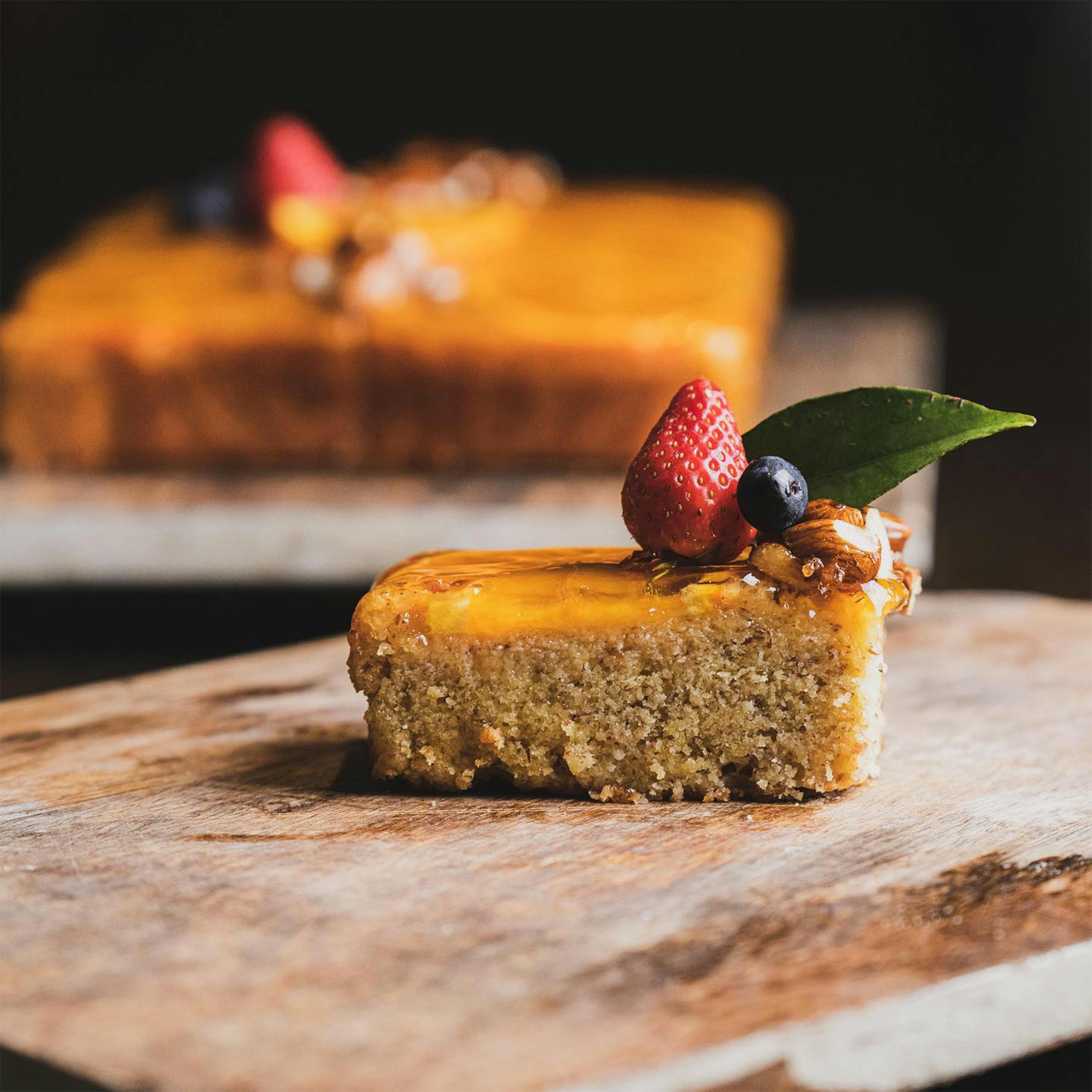 Close-up of a slice of cake topped with strawberries and blueberries on a rustic wooden tray.