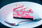 Close-up of a vibrant raspberry cream cake slice with a fork on a plate, perfect for dessert lovers.