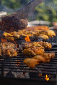 Close-up of barbecue chicken cooking on a grill, surrounded by smoky flames, perfect for summer parties.