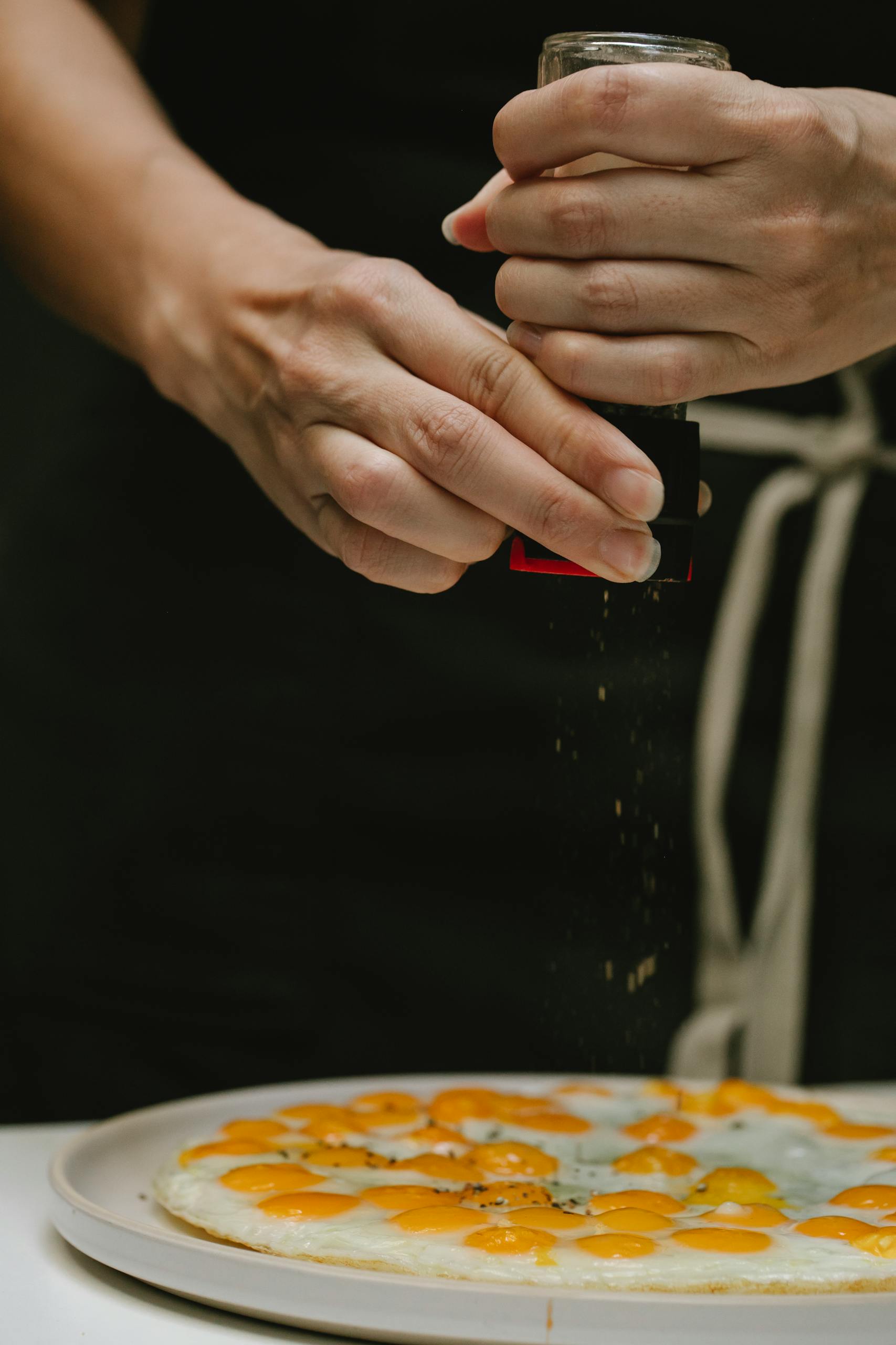 Close-up of chef seasoning a gourmet egg dish with pepper, showcasing culinary expertise.
