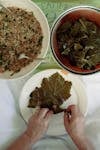 Close-up of hands rolling grape leaves stuffed with rice mixture, a Mediterranean dish.