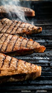Close-up of juicy steaks on a grill with smoke, showcasing ideal grill marks.