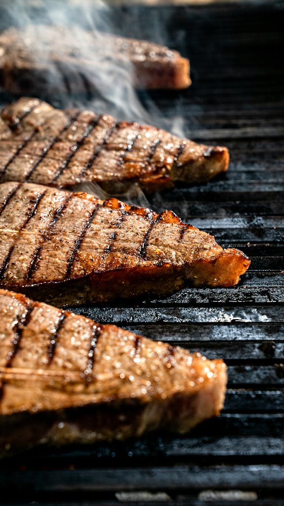 Close-up of juicy steaks on a grill with smoke, showcasing ideal grill marks.