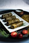 Close-up of traditional stuffed grape leaves on a white plate with fresh herbs and tomatoes.
