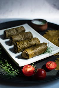 Close-up of traditional stuffed grape leaves on a white plate with fresh herbs and tomatoes.