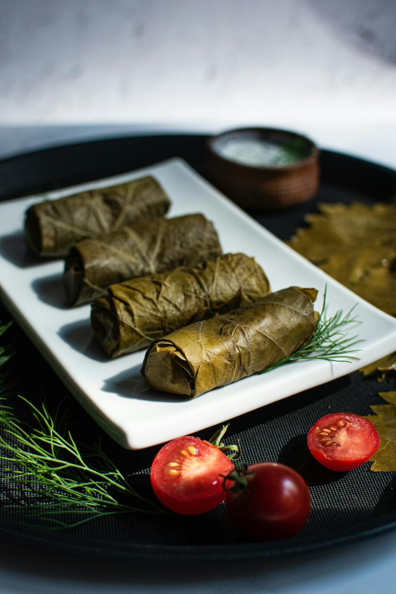 Close-up of traditional stuffed grape leaves on a white plate with fresh herbs and tomatoes.