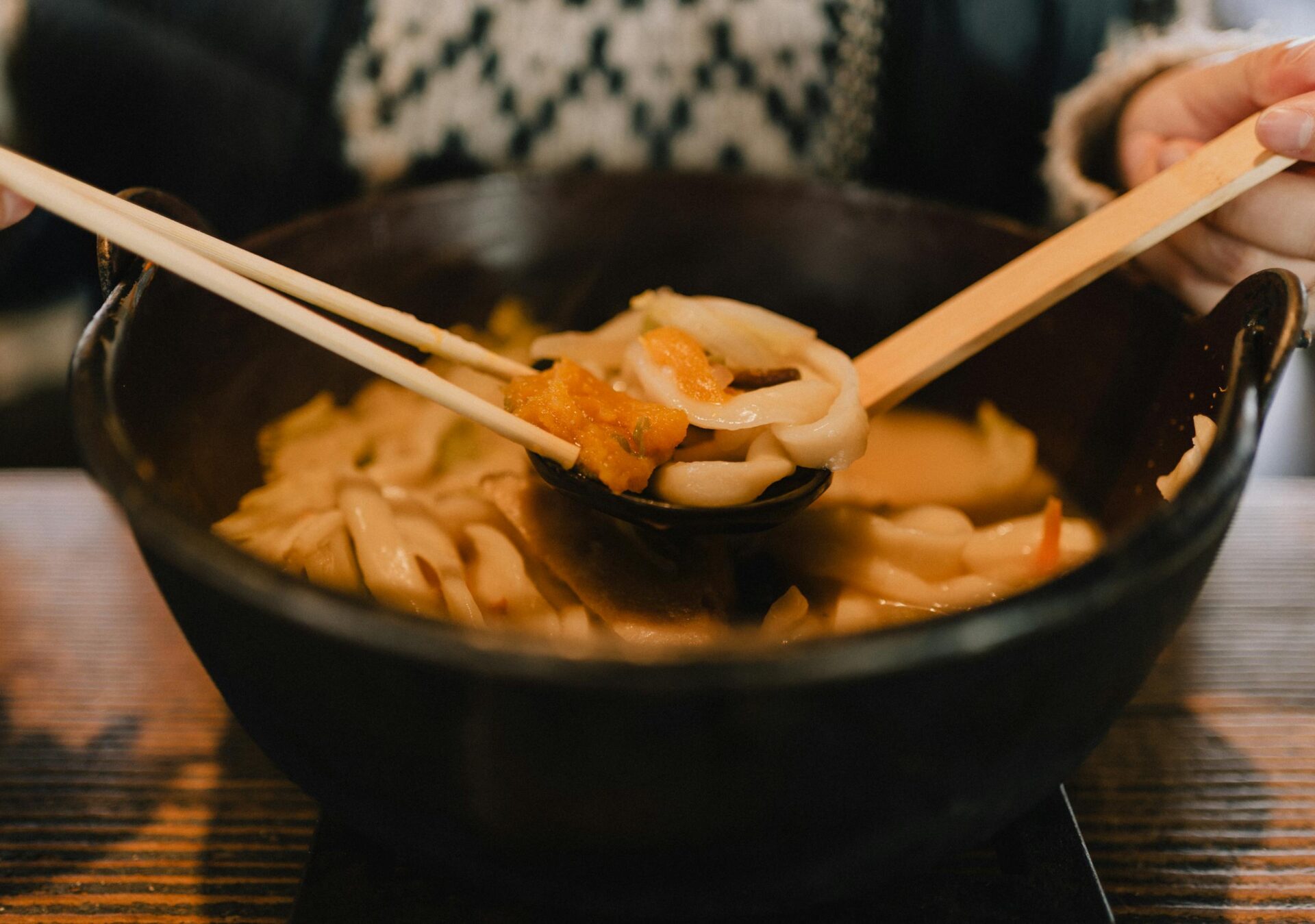 Close-up photo of Japanese udon noodle soup in a dark bowl, served with chopsticks on a table.