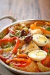 Colorful vegetable and egg dish garnished with olives in a pan.