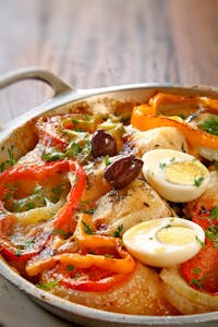 Colorful vegetable and egg dish garnished with olives in a pan.
