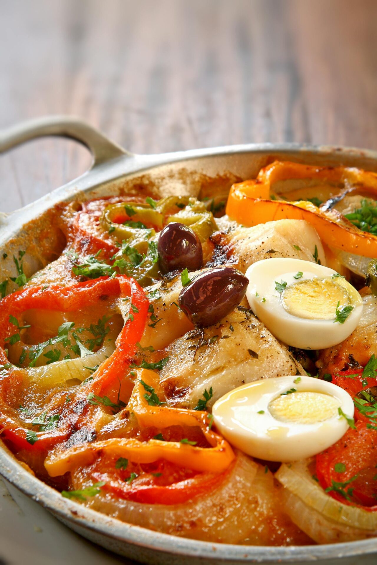 Colorful vegetable and egg dish garnished with olives in a pan.