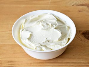 White bowl of creamy dairy spread on a wooden table.