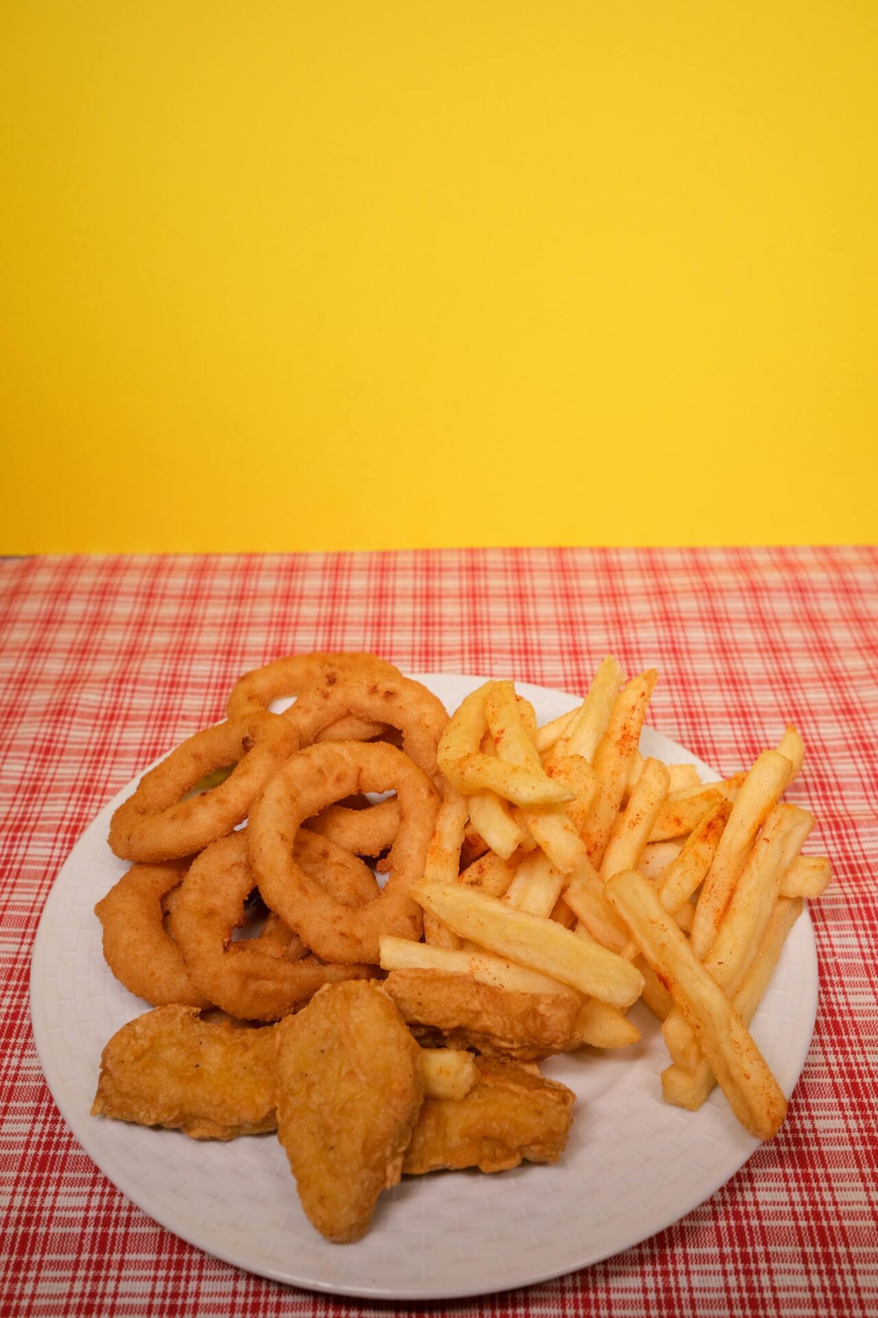 Crispy onion rings, French fries, and nuggets served on a vibrant red plaid tablecloth.