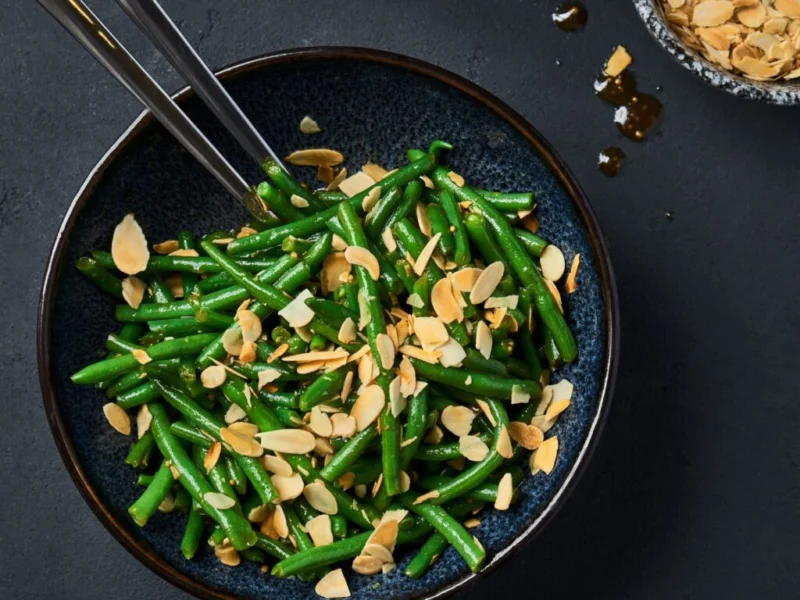 Green beans topped with sliced almonds on a dark plate