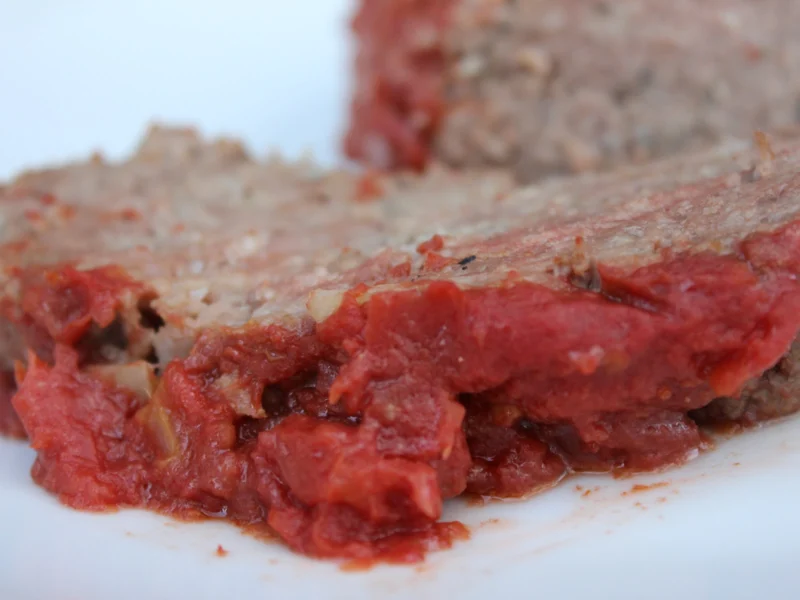Slices of beef meatloaf with a red tomato glaze on a white plate
