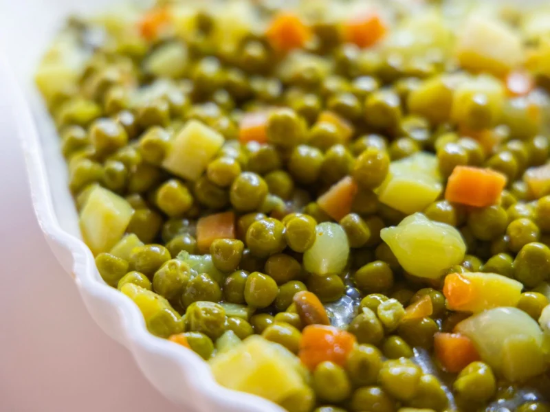 Cooked peas with diced carrots and potatoes in a white serving dish