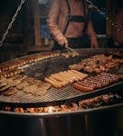 Delicious assortment of German sausages and meats grilling over open flame. Authentic street food vibe.
