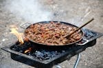 Delicious BBQ meat cooked outdoors on an open fire grill with vibrant peppers.