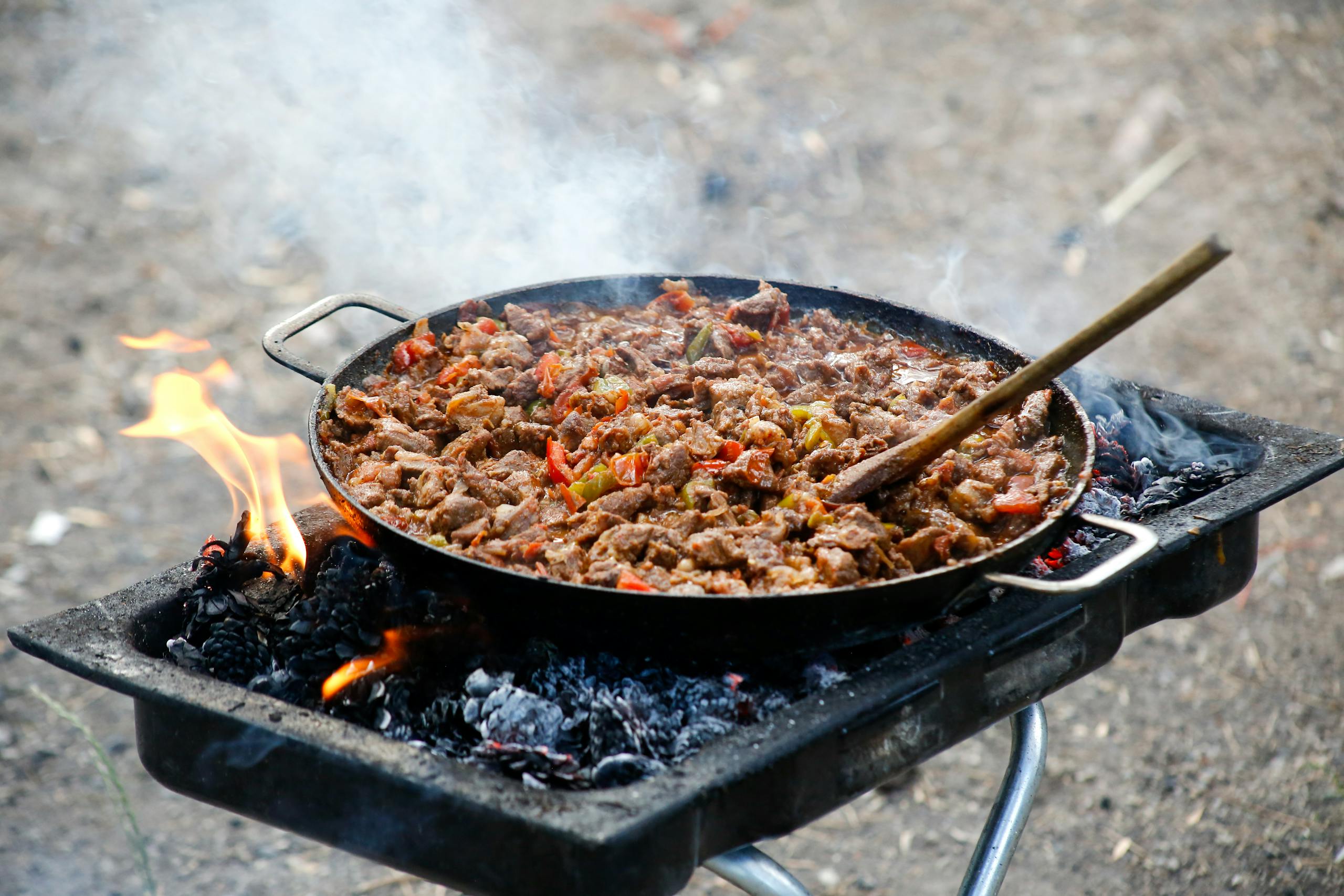 Delicious BBQ meat cooked outdoors on an open fire grill with vibrant peppers.