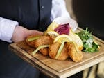 Delicious breaded cutlets served with lemon and greens on a wooden tray in a restaurant.