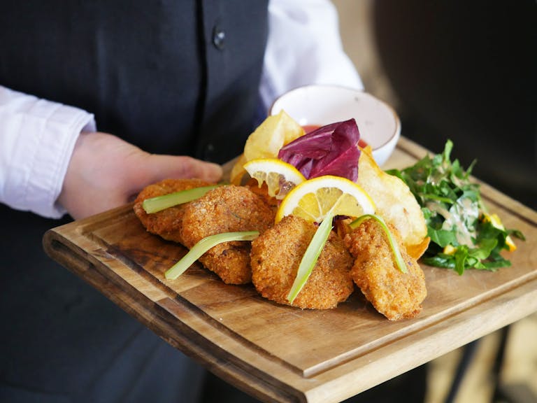 Delicious breaded cutlets served with lemon and greens on a wooden tray in a restaurant.