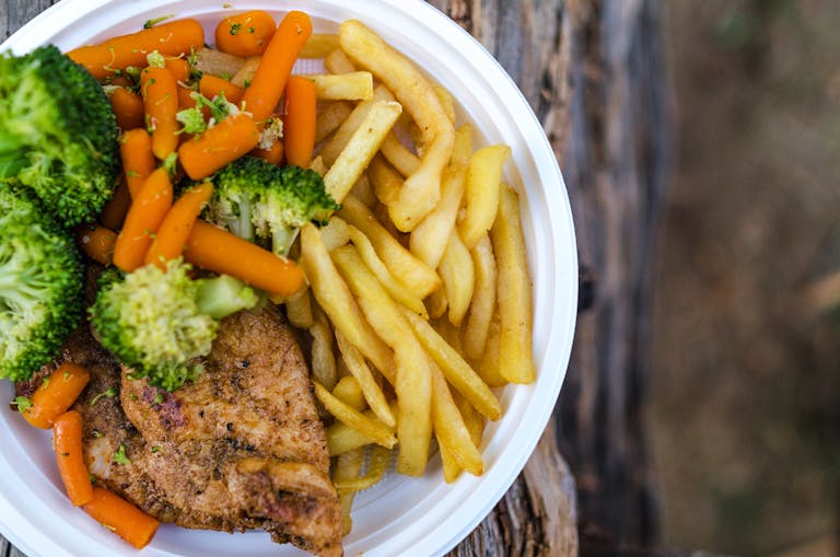 Delicious chicken dinner with broccoli, carrots, and fries on a plate.