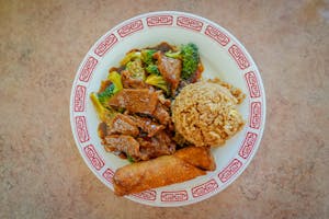Delicious Chinese beef and broccoli with fried rice and egg roll on a decorative plate.