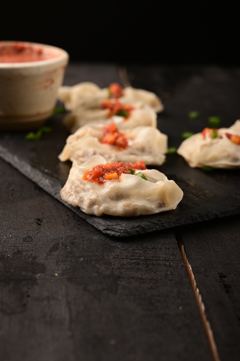 Delicious dumplings topped with spicy sauce on a dark wooden tray, ready to eat.
