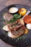 Delicious gourmet meat dish served with grilled vegetables and herbs on a black plate.