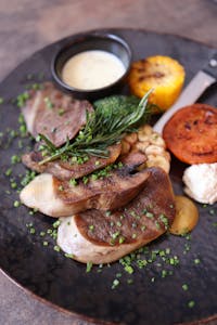Delicious gourmet meat dish served with grilled vegetables and herbs on a black plate.
