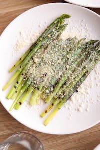 Delicious grilled asparagus topped with parmesan cheese on a white plate.