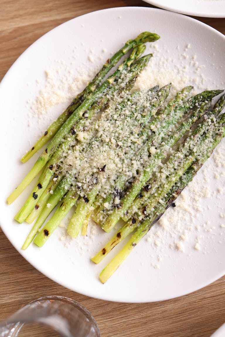 Delicious grilled asparagus topped with parmesan cheese on a white plate.