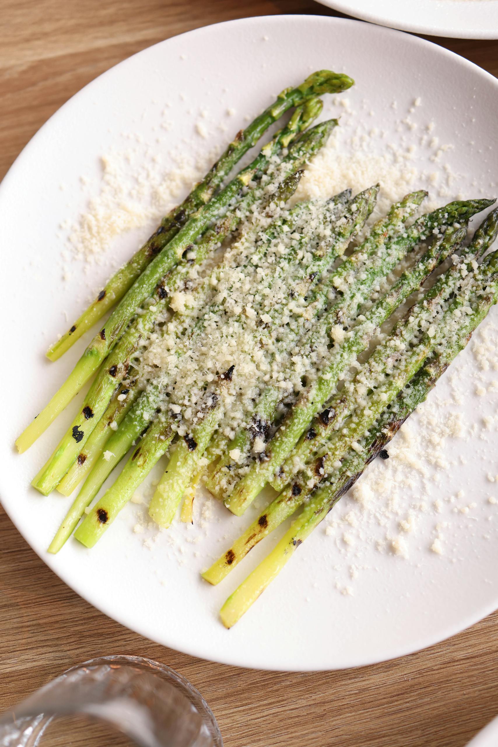 Delicious grilled asparagus topped with parmesan cheese on a white plate.