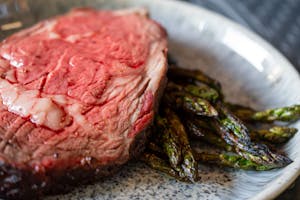 Delicious grilled steak paired with roasted asparagus served on a ceramic plate.
