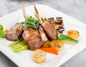 Delicious lamb chops with vegetables plated elegantly on a marble surface.
